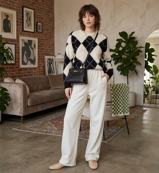 Woman in a black and white patterned sweater and white pants standing in a stylish living room.