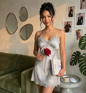 Woman in a white lace nightgown holding a red rose and a book, standing in a room with decor elements.