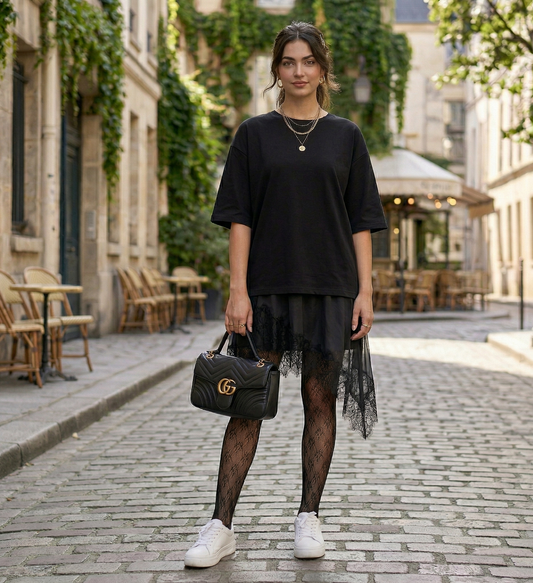 Woman in black outfit with lace skirt and white sneakers standing on a street.