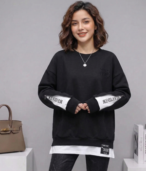 Woman wearing a black sweatshirt with white text on sleeves against a gray background