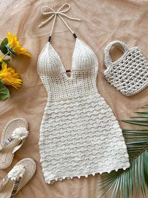 White crochet dress with matching bag on a beige surface with sunflowers and sandals.