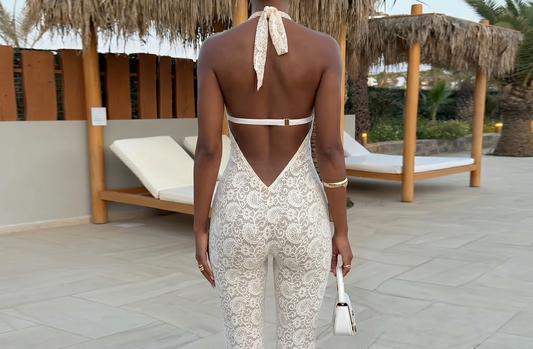 Woman in a white lace outfit standing on a patio with lounge chairs and palm trees.
