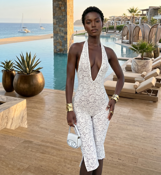 Woman in a white lace dress standing by a poolside with ocean view