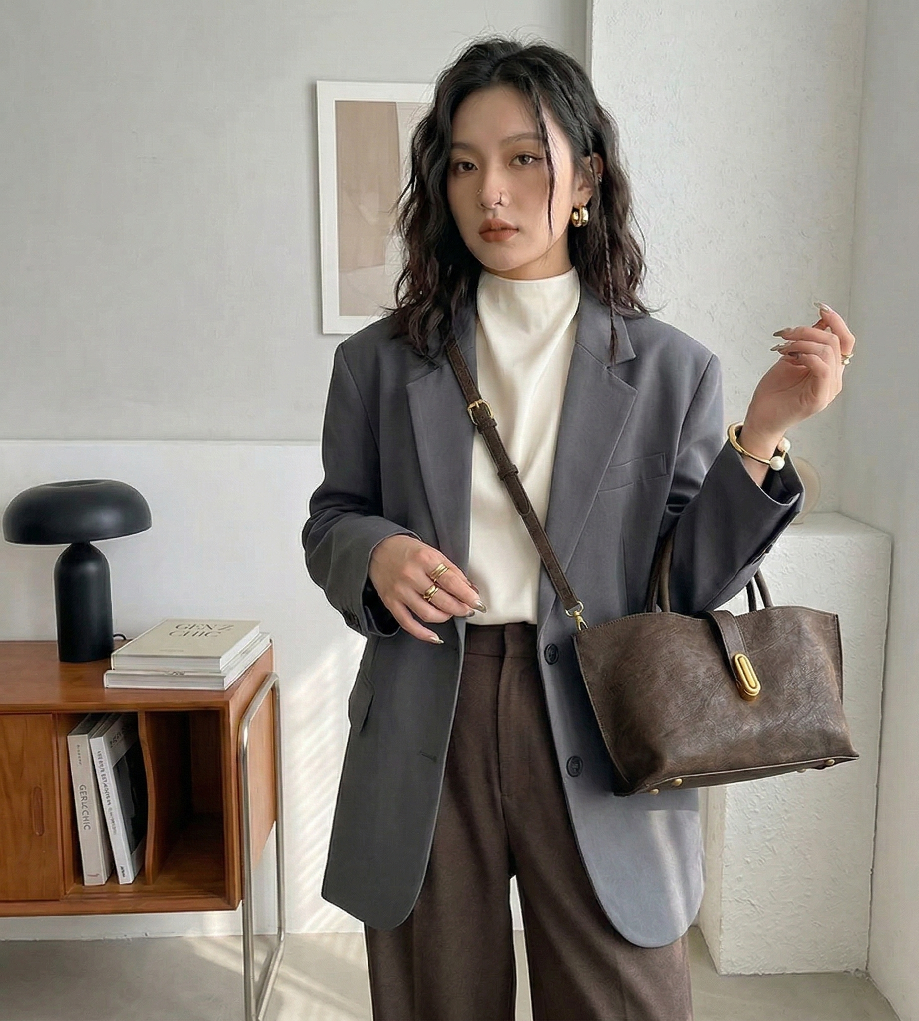 Woman holding a brown handbag in a room with a lamp and books on a shelf.