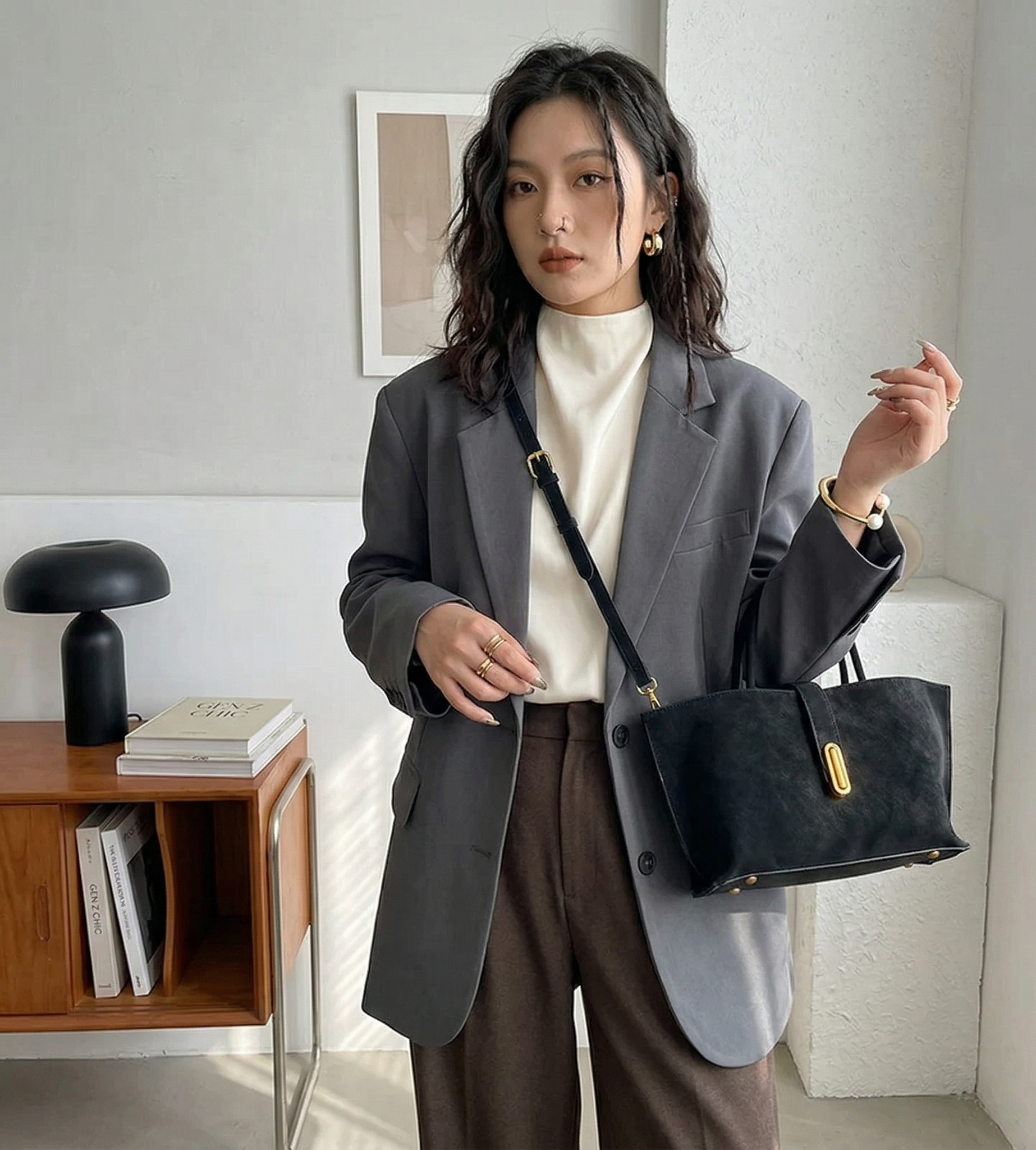 Woman holding a black handbag in a room with a lamp and books on a table.