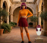 Person wearing a yellow top and red skirt standing in an outdoor setting with a wig on a mannequin head.