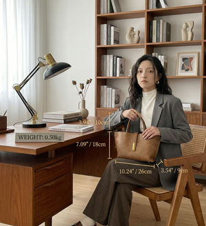Woman holding a brown handbag in an office setting with a desk and bookshelf.