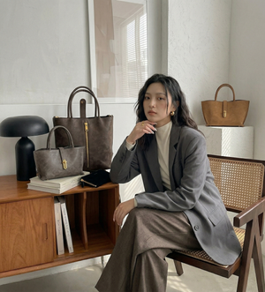 Woman in a gray coat sitting in a chair with handbags displayed around her.