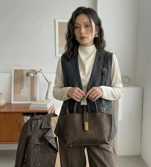 Woman holding a brown handbag in a room with a desk and lamp.
