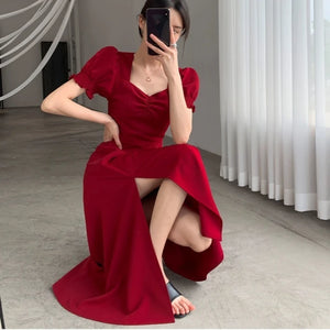 Woman in a red dress posing in a room with white curtains.