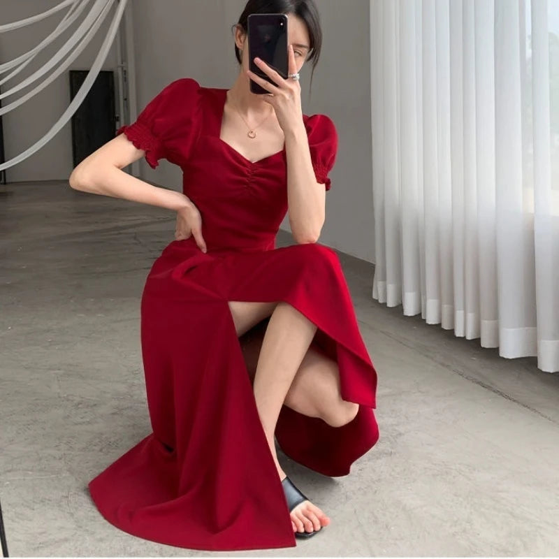 Woman in a red dress posing in a room with white curtains.